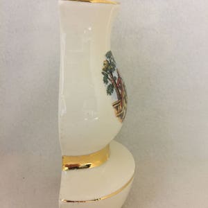 May include: A white ceramic vase with a gold trim and a painted scene of a couple in a garden. The vase is shaped like a traditional pitcher with a wide base and a narrow neck.