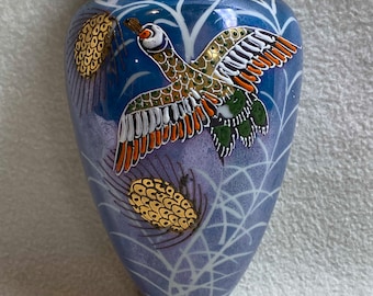 May include: A blue and white ceramic wall vase with a gold rim and a painted design of a bird in flight. The vase has a textured surface and a delicate, intricate design.