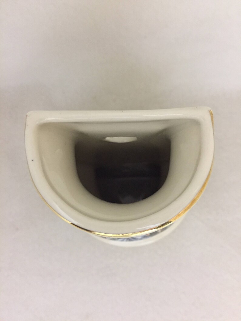 May include: A white ceramic toothbrush holder with a gold rim. The holder has a single opening for a toothbrush.