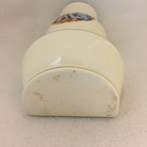 May include: A white ceramic vase with a gold rim and a floral design. The vase is shaped like a bottle and has a rounded bottom.