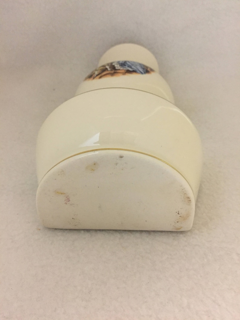 May include: A white ceramic vase with a gold rim and a floral design. The vase is shaped like a bottle and has a rounded bottom.