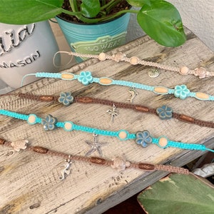 May include: Five turquoise and brown friendship bracelets with various sea-themed charms, including a starfish, a seahorse, a turtle, a dolphin, and a palm tree. The bracelets are made with knotted string and wooden beads.