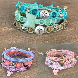 May include: Three sets of layered bracelets with cross charms. The first set is turquoise, green, and brown. The second set is purple, pink, and orange. The third set is pink and white.