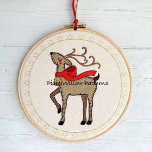 May include: Embroidered Christmas reindeer with a red scarf and a bell, in a wooden embroidery hoop with a gold star pattern.