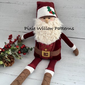 May include: A plush Santa Claus doll with a red velvet suit, white fur beard, and brown boots. The doll is sitting on a white wooden surface with a sprig of holly and berries.