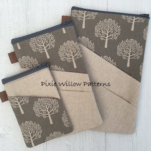 Könnte beinhalten: Drei Reißverschlusstaschen in verschiedenen Größen mit einem braunen und beigefarbenen Baummuster. Die Taschen sind aus Stoff und haben einen braunen Leder-Reißverschluss. Die größte Tasche hat eine beigefarbene Leinenklappe mit einer Tasche. Die Taschen sind auf einer weißen Holzoberfläche angeordnet. Der Text "Pixie Willow Patterns" ist auf den Taschen aufgedruckt.