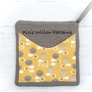 May include: Gray quilted pot holder with a yellow fabric pocket featuring a floral pattern. The pot holder has a gray loop for hanging. The text "Pixie Willow Patterns" is embroidered on the gray fabric.