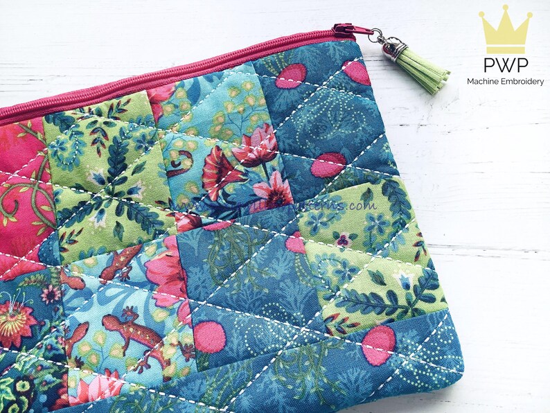 May include: A quilted zippered pouch with a patchwork design featuring floral and geometric patterns in shades of pink, green, and blue. The pouch has a light pink zipper and a green tassel.
