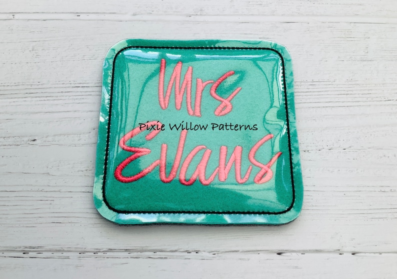 May include: A teal blue square patch with a black border and the text "Mrs. Evans" in pink cursive lettering. The text "Pixie Willow Patterns" is also included in black lettering.