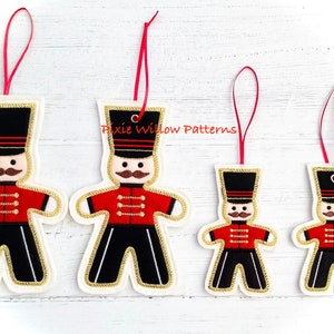 May include: Four felt Christmas ornaments in the shape of a gingerbread soldier. The ornaments are red, black, white, and gold. The ornaments have a red ribbon for hanging.