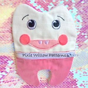 Pode incluir: Um brinquedo de pelúcia branco em forma de dente com uma bolsa com zíper rosa. O brinquedo tem olhos bordados, uma boca rosa e o texto "Pixie Willow Patterns" na bolsa.