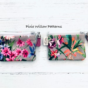 May include: Two small zippered pouches with floral patterns. The pouch on the left has a pink and white floral pattern. The pouch on the right has a tropical floral pattern. Both pouches have a white zipper and a pink tassel.