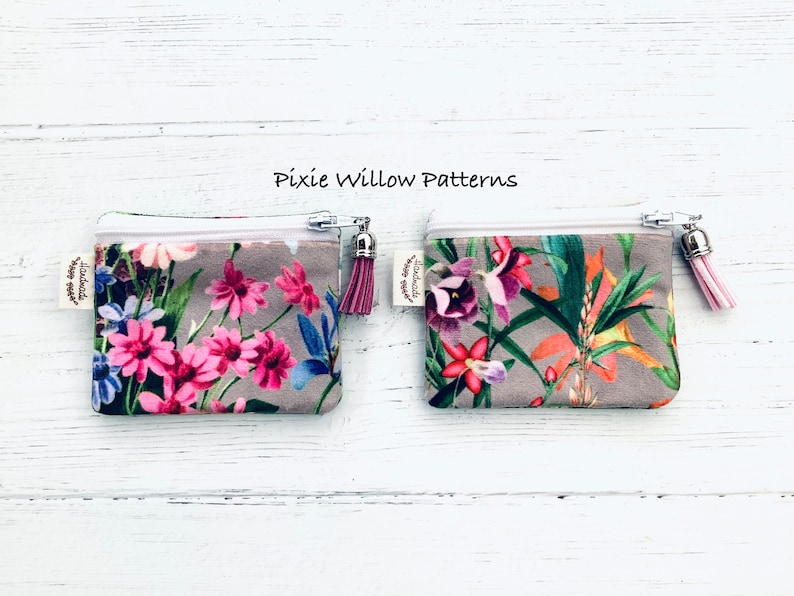 May include: Two small zippered pouches with floral patterns. The pouch on the left has a pink and white floral pattern. The pouch on the right has a tropical floral pattern. Both pouches have a white zipper and a pink tassel.