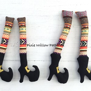 May include: Four pairs of witch legs with black boots and colorful patterned fabric. The fabric has a geometric pattern with orange, yellow, green, and purple colors. The boots have a pointed toe and a gold buckle. "Pixie Willow Patterns" is written on the fabric.