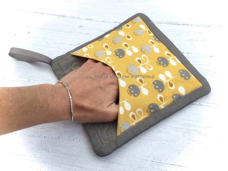 May include: A gray and yellow pot holder with a floral pattern and a loop handle. The pot holder has a pocket on the front. "Pixie Willow Patterns" is printed on the front of the pot holder.