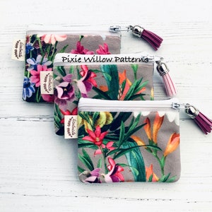 May include: Two small zippered pouches with floral patterns and tassels. The pouches are made of a soft, gray fabric with a white zipper. The pouches are labeled "Handmade with love".
