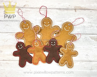 May include: Six felt gingerbread people ornaments in various sizes, with brown and tan felt, red stitching, and white smiling faces. The ornaments are hanging from red and white twine on a light wood background.