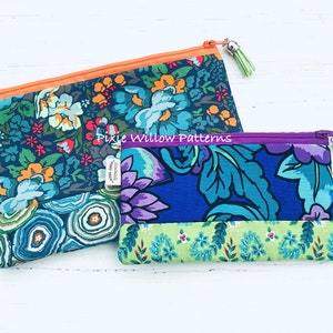Op de afbeelding: Twee ritszakjes met bloemenpatronen. Het grotere zakje heeft een blauw, groen en oranje bloemenpatroon met een lichtoranje rits. Het kleinere zakje heeft een blauw, groen en paars bloemenpatroon met een paarse rits. Beide zakjes hebben een rits met een kwast.