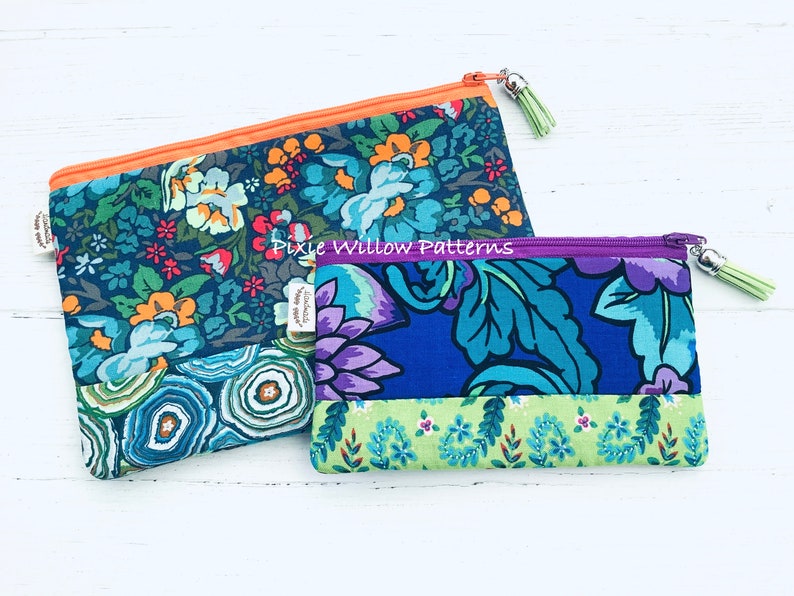 Op de afbeelding: Twee ritszakjes met bloemenpatronen. Het grotere zakje heeft een blauw, groen en oranje bloemenpatroon met een lichtoranje rits. Het kleinere zakje heeft een blauw, groen en paars bloemenpatroon met een paarse rits. Beide zakjes hebben een rits met een kwast.