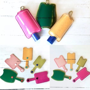 May include: A set of six hand sanitizer holders in various colors, including green, pink, yellow, and brown. The holders are made of fabric and have a loop for attaching to a keychain. The holders are designed to fit small hand sanitizer bottles. The text "Pixie Willow Patterns" is visible on some of the holders.