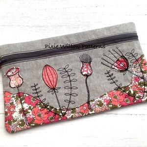 Puede incluir: Una bolsa de cremallera gris con un diseño floral bordado en la parte delantera. El diseño presenta flores rosas y rojas con tallos y hojas negras. El texto "Pixie Willow Patterns" está bordado en la parte superior de la bolsa.