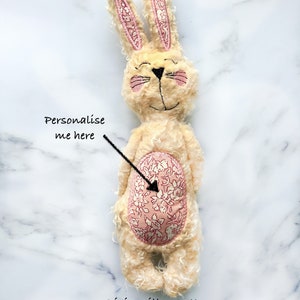 May include: A cream-coloured plush bunny with pink detailing on the ears and cheeks. The bunny features a floral patterned patch on its belly. The image includes the text "Personalise me here" and "Pixie Willow Patterns".