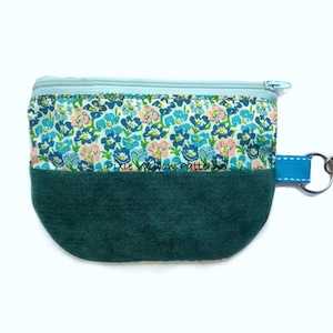 May include: A small, teal blue zippered pouch with a floral print and a teal blue fabric bottom. The pouch has a blue ribbon attached to a silver key ring.