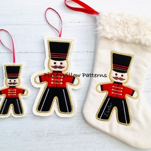 May include: Three felt Christmas ornaments featuring a gingerbread man dressed as a toy soldier. The ornaments are in different sizes. The largest ornament is on a white stocking with a faux fur cuff. The stocking is personalized with the name "Dexter".