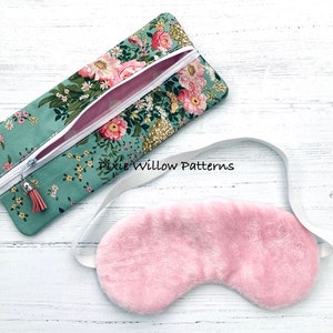 May include: A teal zippered pouch with a floral print and a pink tassel. A pink sleep mask with a white elastic strap is next to the pouch. The text "Pixie Willow Patterns" is visible on the pouch.