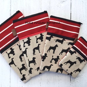 May include: Set of four zippered pouches with red and white striped fabric and a linen fabric with black silhouettes of dogs. The largest pouch has the text "Pixie Willow Patterns" printed on it.