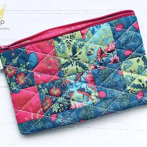 May include: A pink and blue quilted zippered pouch with a floral and geometric pattern. The pouch is made of fabric and has a white stitching detail.