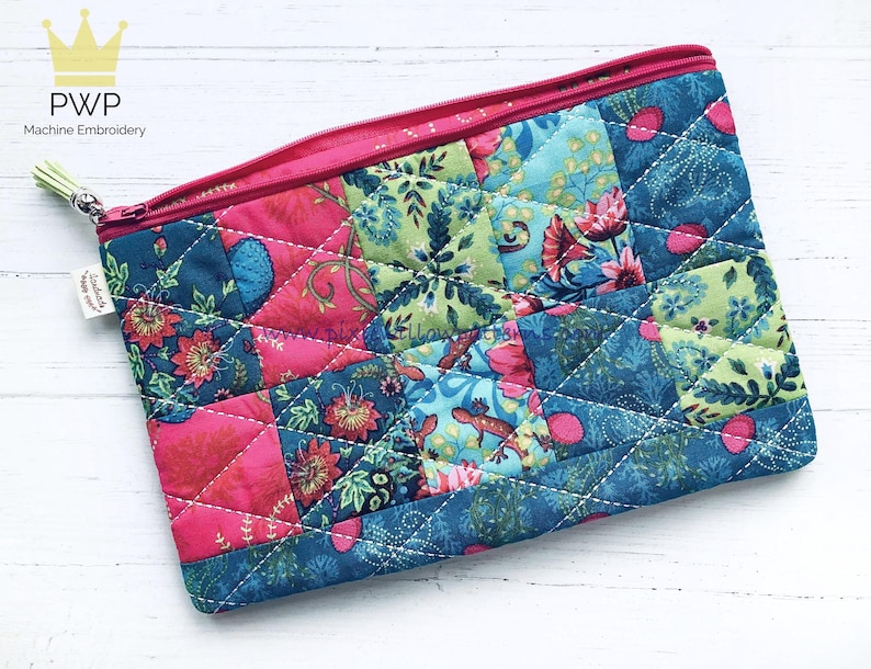 May include: A pink and blue quilted zippered pouch with a floral and geometric pattern. The pouch is made of fabric and has a white stitching detail.