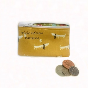 May include: A small yellow zippered pouch with a white zipper and a white background with a repeating pattern of white dogs with black noses and eyes. The pouch has the text "Pixie Willow Patterns" printed on the front.