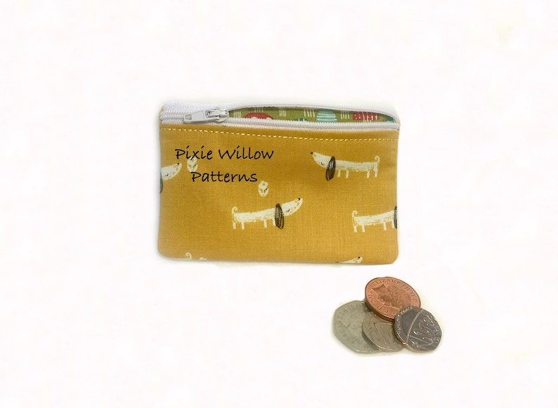 May include: A small yellow zippered pouch with a white zipper and a white background with a repeating pattern of white dogs with black noses and eyes. The pouch has the text "Pixie Willow Patterns" printed on the front.