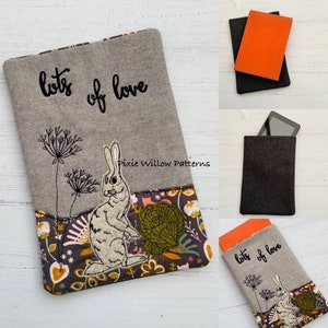 Könnte beinhalten: Graue Tablethülle mit einem gestickten Hasen- und Blumenmuster. Der Text "lots of love" ist in Schwarz gestickt. Der untere Teil hat einen gemusterten Stoff mit Blumen und Blättern. Entworfen für ein Tablet oder einen E-Reader.