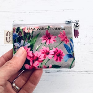 May include: A small floral print zipper pouch with a pink tassel. The pouch has a white zipper and a silver charm. The pouch is handmade and says "Pixie Willow Patterns" on the front.