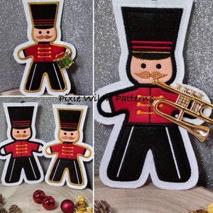 May include: Three felt ornaments shaped like gingerbread men, one playing a trumpet, one holding a drum, and one with no instrument. The ornaments are decorated with red, black, and gold details. The ornaments are on a white background.
