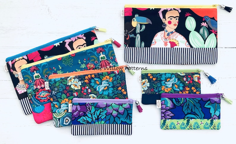 Op de afbeelding: Een set van zes kleurrijke ritszakjes met verschillende bloemen- en Frida Kahlo-ge&iuml;nspireerde ontwerpen. De zakjes zijn gemaakt van stof en hebben een zwart-wit gestreepte onderkant. De tekst "Pixie Willow Patterns" is zichtbaar op een van de zakjes.