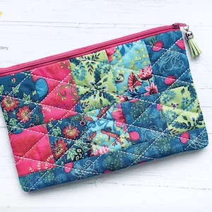 May include: A pink and blue quilted zippered pouch with a floral pattern. The pouch has a small tassel zipper pull.