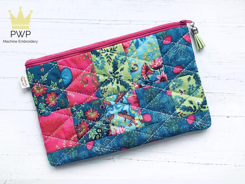 May include: A pink and blue quilted zippered pouch with a floral pattern. The pouch has a small tassel zipper pull.