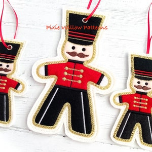 May include: Three felt Christmas ornaments shaped like gingerbread men, each wearing a red and black uniform with gold trim. The ornaments are decorated with gold buttons and a black hat with gold trim. The largest ornament is approximately 6 inches tall, the middle ornament is approximately 4 inches tall, and the smallest ornament is approximately 3 inches tall.