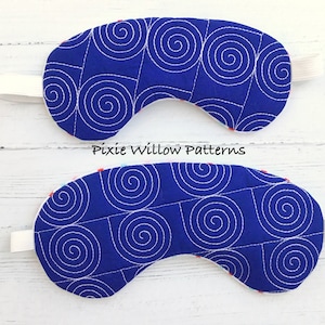 May include: Two blue sleep masks with white spiral patterns. The masks are made of fabric and have elastic straps. The text "Pixie Willow Patterns" is printed on the white surface below the masks.