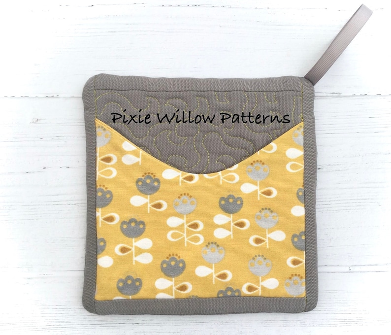 May include: Gray quilted pot holder with a yellow fabric pocket featuring a floral pattern. The pot holder has a gray loop for hanging. The text "Pixie Willow Patterns" is embroidered on the gray fabric.