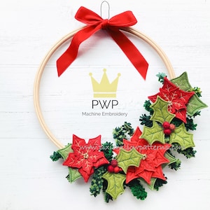Może przedstawiać: Wianek bożonarodzeniowy z czerwonymi gwiazdami betlejemskimi i zielonym ostrokrzewem wyszywanym na drewnianym obręczy z czerwoną wstążką. Wianek jest ozdobiony złotym brokatem i czerwonymi jagodami. Wianek jest oznaczony "PWP Machine Embroidery".