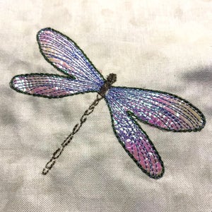 May include: A purple and green embroidered dragonfly with iridescent wings on a white fabric background.