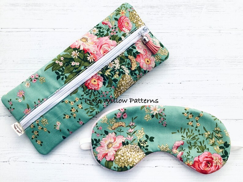 May include: A green floral print eye mask and matching zipped pouch. The pouch has a white zipper and a pink tassel. The text "Pixie Willow Patterns" is printed on the pouch.