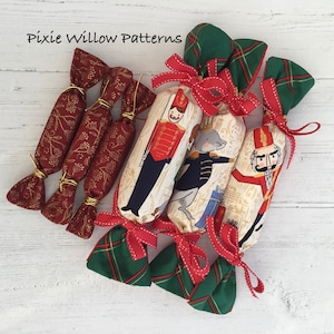 Puede incluir: Un conjunto de seis crackers navideños hechos a mano con una tela roja y dorada con un patrón floral y una tela de cuadros verde y roja con una ilustración de un cascanueces y un ratón. Los crackers están atados con una cinta roja y un alambre dorado.