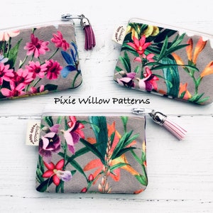 May include: Three small zippered pouches with floral patterns and tassels. The pouches are made of a soft, gray fabric with a white zipper. The tassels are pink, red, and white. The pouches are labeled "Pixie Willow Patterns".
