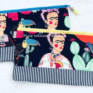 Op de afbeelding: Twee zwarte ritsen met een kleurrijke Frida Kahlo- en toekanprint. De portemonnees hebben een zwart-wit gestreepte onderkant en gele ritsen.