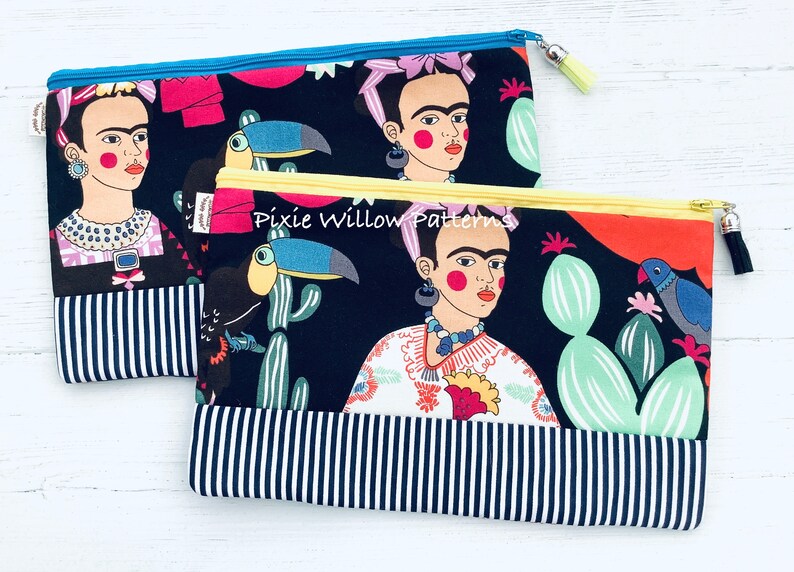 Op de afbeelding: Twee zwarte ritsen met een kleurrijke Frida Kahlo- en toekanprint. De portemonnees hebben een zwart-wit gestreepte onderkant en gele ritsen.